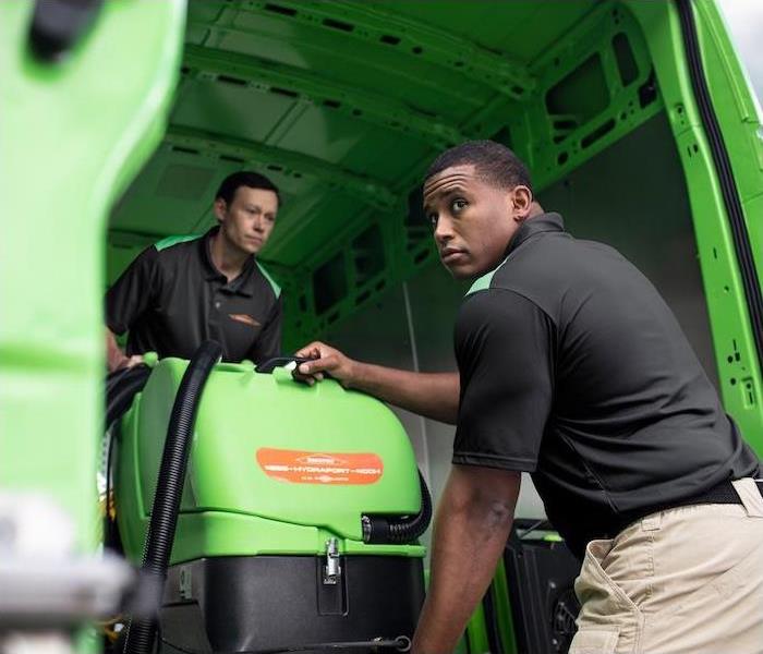 "two SERVPRO employees unloading cleaning equipment out of a green van"   